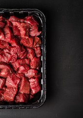 Closeup Raw sliced beef meat in plastic container on dark background. Background with copy space. Selective focus. Top view
