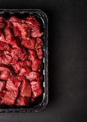 Closeup Raw sliced beef meat in plastic container on dark background. Background with copy space. Selective focus. Top view