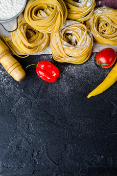 Homemade pasta with rolling pin, flour, tomato and peppers on dark background. Top view, copy space. Selective focus