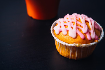 cupcake with pink frosting and red cup on a wooden background
