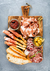 Meat appetizer selection or wine snack set. Variety of smoked meat, salami, prosciutto, bread sticks, baguette, olives and sun-dried tomatoes over grey concrete textured backdrop