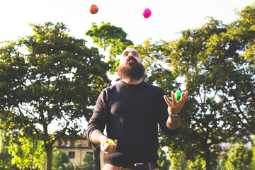 long bearded millennial bald  man juggling with balls at the park