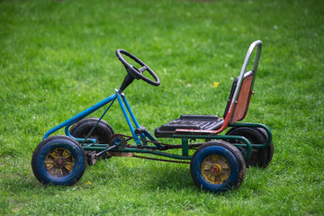 Old children's car, standing on green grass in the rain. isolate