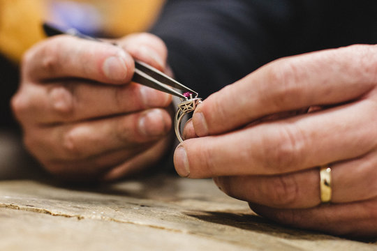 Close-up of a jeweller sitting at a table mounting a precious gemstone onto a gold ring