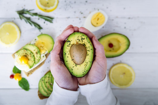 Overhead view of a person holding half an avocado over a table with avocado and egg sandwiches