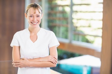 Portrait of happy female masseur with arms crossed standing at health spa