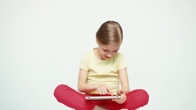 Girl 7-8 years old using tablet pc and sitting on the floor on white background