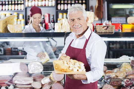 Happy Man Holding Various Cheese On Board In Store