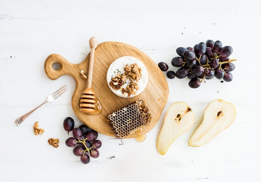 Camembert cheese with grape, walnuts, pear and honey on oak serving board