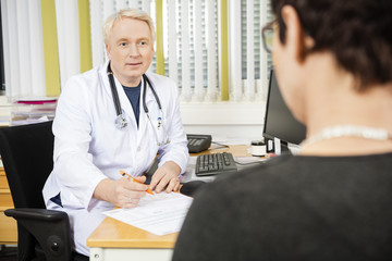 Fototapeta premium Male Doctor Writing Prescription For Female Patient At Desk