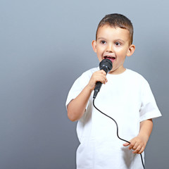 Cute little boy kid singing on microphone against gray backgroun