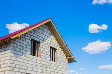 house under construction from aerated concrete blocks. unfinished house with a red roof against the blue sky and clouds. copy space for your text