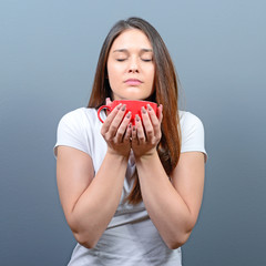 Woman enjoying aroman of hot beverage against gray background