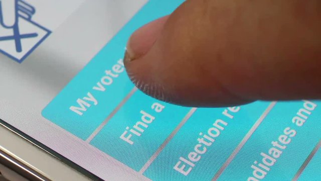 Macro close up of a smartphone / tablet, with camera moving down to settle on section 'Find a Voting Station'. User taps with finger, leading to 2nd screen.