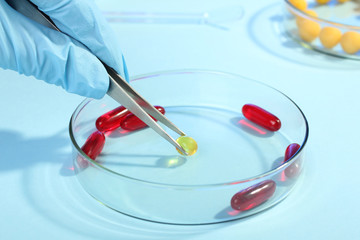 the doctor pulls the pill with tweezers from the Petri bowl on a wooden table