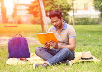 Young indian man reading book in park outdoors 
