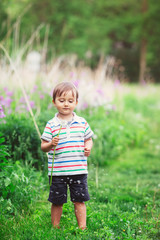 Portrait of a cute funny little boy toddler standing in the forest field meadow with dandelion flowers in hands and blowing them on a bright summer day, summer fun, copyspace for text