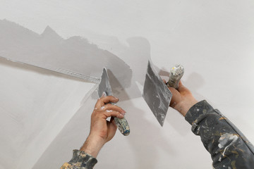 Worker repairing plaster at ceiling, install corner protecting batten