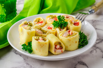 Pancakes rolls stuffed ham, pepper and salad, in bowl on marble background. 