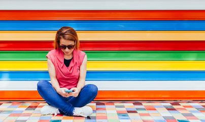 Young woman using a smartphone in front of the colorful wall