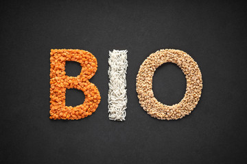 Wort BIO als Schriftzug aus roten Linsen, Basmati-Reis und Urdbohnen auf dunklem Hintergrund gelegt