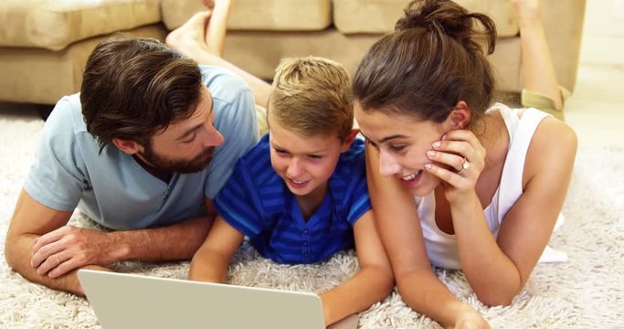 Happy family looking a laptop lying on a carpet