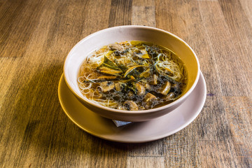 Noodle soup with forest mushrooms, chicken white meat and vegetables on wooden background