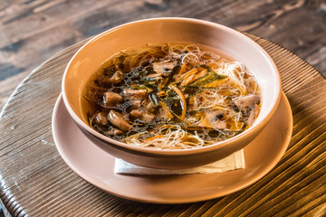 Noodle soup with forest mushrooms, chicken white meat and vegetables on wooden background