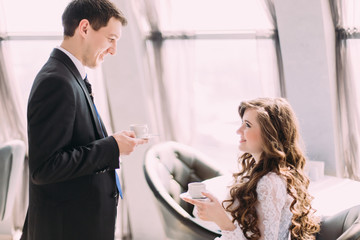 Handsome young groom in black suit brings his bride coffee