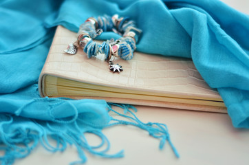 Photo album lies on a white background. Blue scarf covers album. Bracelet in marine style lies on the album.