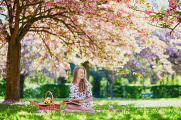 Girl having picnic and reading book in cherry garden