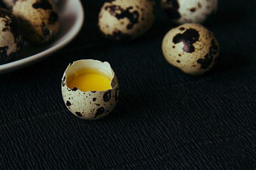 Quail eggs on a black textured background. Raw broken egg with the yolk. Easter card. Side view....