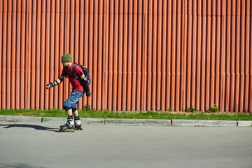 Guy rides on roller skates on an asphalt track against the red wall