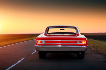 Obraz na płótnie Canvas Retro red car standing on asphalt road at sunset
