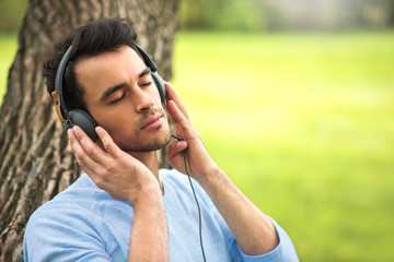 Portrait of beautiful man with headphones, listen music on the tree background.