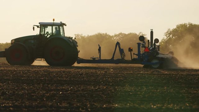The tractor sows a field at sunset. The sun's rays near the beautiful light drills
