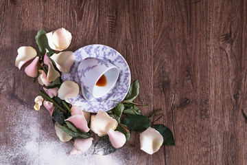 Overturned tea cup on a wooden table among flower leaves and petals. Top view.