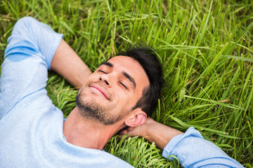 Beautiful young man with closed eyes, dreaming and relax on the green grass