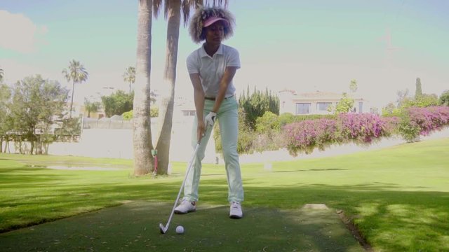 Attractive woman golfer playing a shot lining up her ball with the flag in the hole  close up view with urban backdrop in the distance
