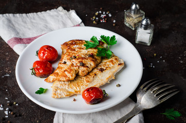 Roasted turkey steak with tomatoes, parsley and spice in white bowl on dark slate background. Selective focus. Toned image