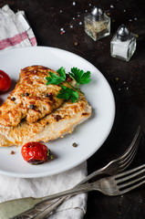 Roasted turkey steak with tomatoes, parsley and spice in white bowl on dark slate background. Selective focus. Toned image