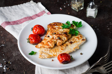 Roasted turkey cutlet or steak with tomatoes in white bowl on dark slate background. Selective focus