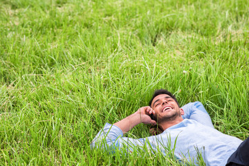 Naklejka na ściany i meble Happy dreaming young business man lying on the green grass. Talking on the telephone