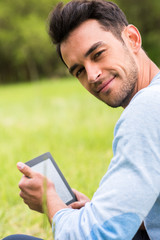 Pretty smiling young business man with device look at the camera on nature green background