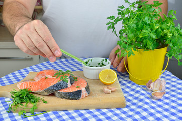 Preparing salmon steaks for baking. Spicing with salt, lemon, parsley, oil, garlic...