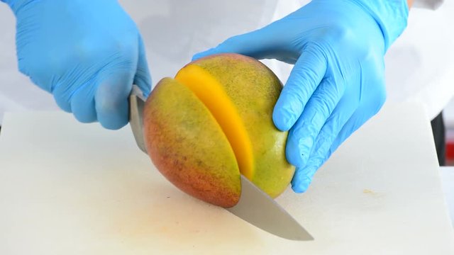 Hands of chef cutting a mango fruit in small dices with a knife in the kitchen for a recipe
