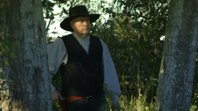 A cowboy from the American wild west era observes something that causes him to draw his black powder pistol.