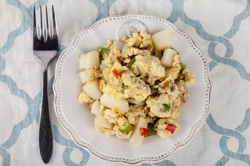 Scrambled eggs with Anaheim chilies, boiled potatoes, green peppers, and onions top view on a blue and white place mat