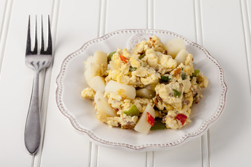 Scrambled eggs with Anaheim chilies, boiled potatoes, green peppers, and onions on white wood