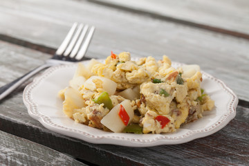Scrambled eggs with Anaheim chilies, boiled potatoes, green peppers, and onions on a weathered barn wood table
